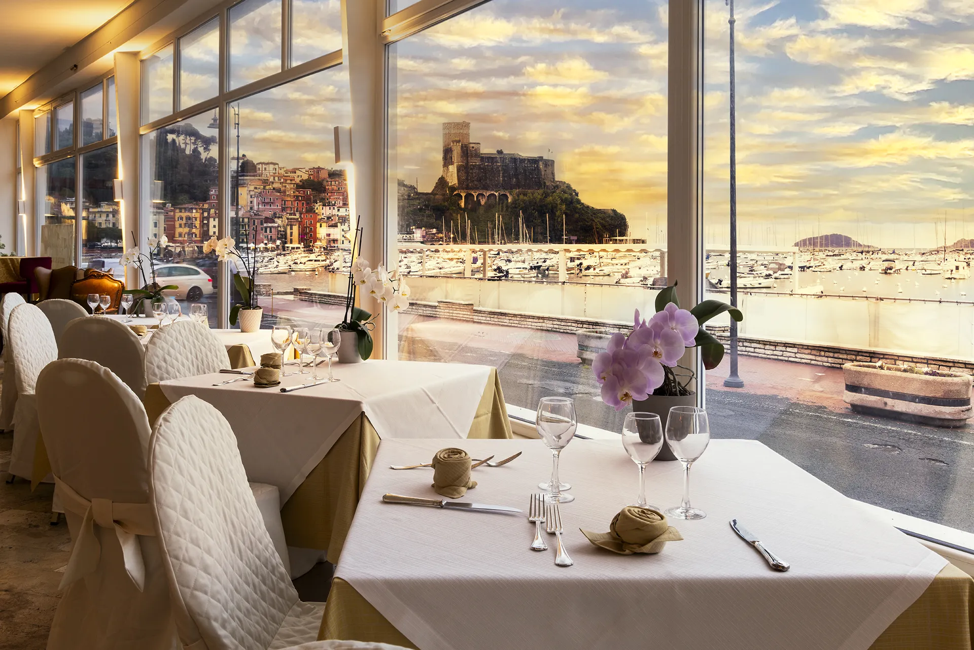 Nell'immagine, il ristorante dell'Hotel Shelley e Delle Palme al tramonto, con alcuni tavoli apparecchiati davanti a una vetrata con vista sul mare e il castello.