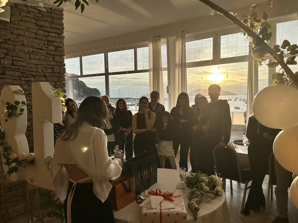 Nell'immagine, una ragazza di spalle sta aprendo dei regali per il suo diciottesimo compleanno di fronte alla famiglia.